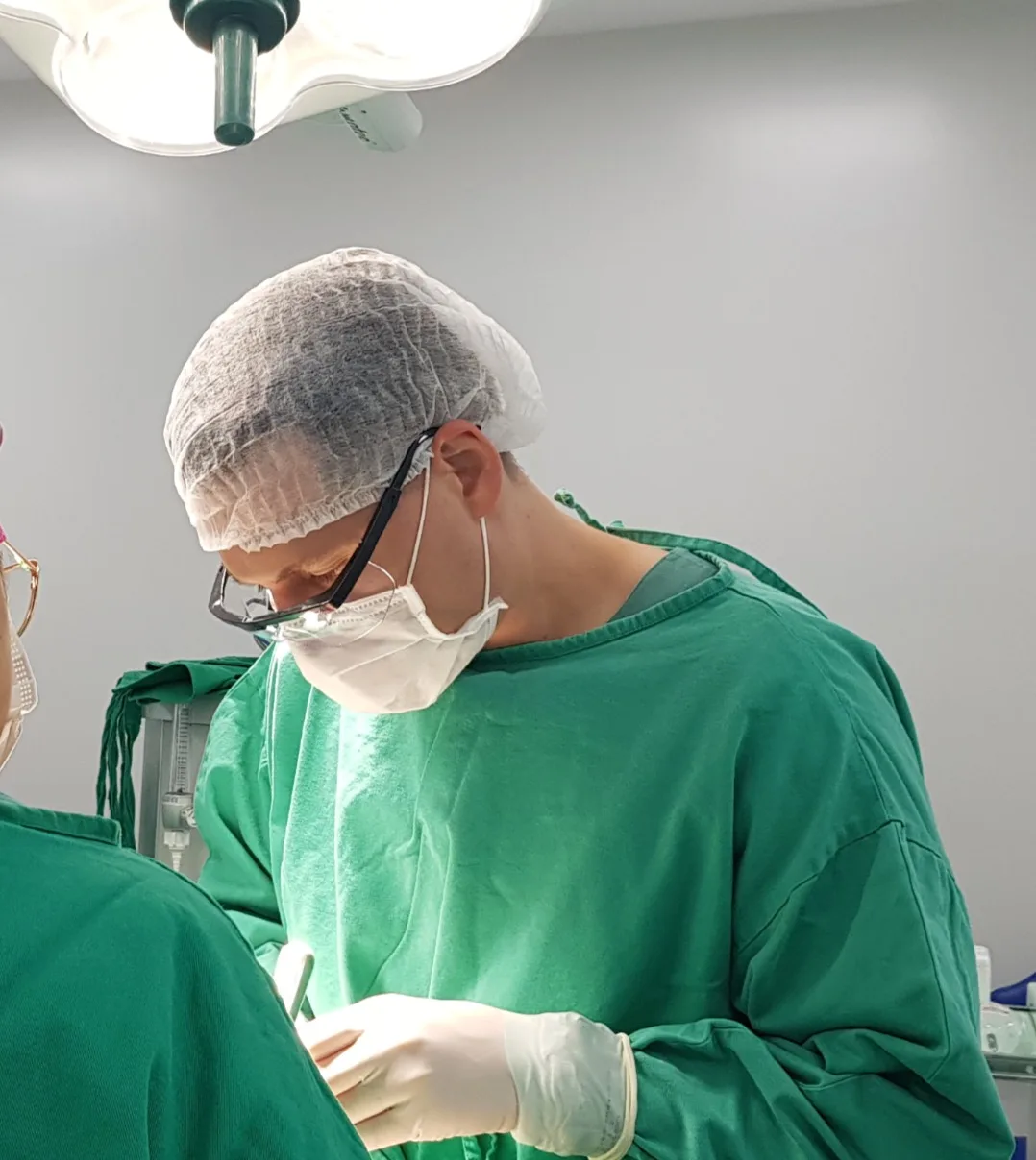 Cirurgião de touca, máscara e avental verde operando sob o foco do centro cirúrgico